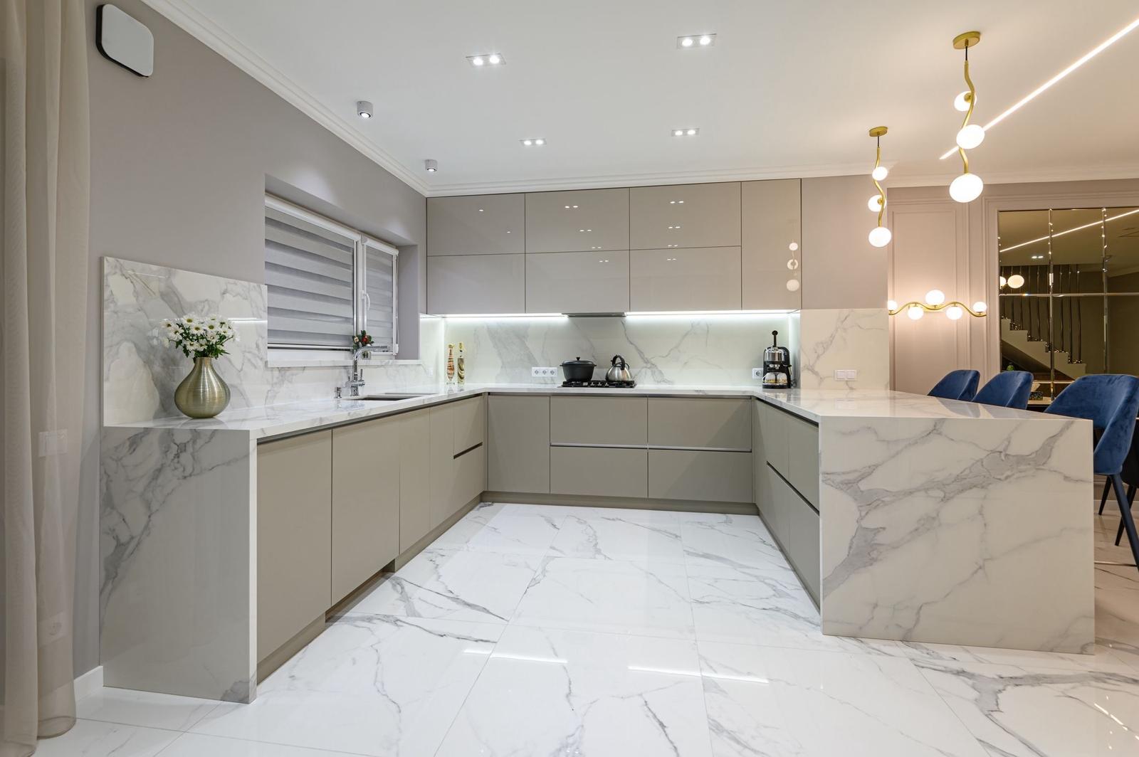 Expansive modern kitchen featuring a large white marble island with gold vein detailing, sleek handleless cabinetry in a matte finish, and three pendant lights hanging above the workspace.